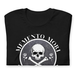 May include: Black t-shirt with a white skull and crossbones design. The design includes the words "Memento Mori" in a circle around the skull.