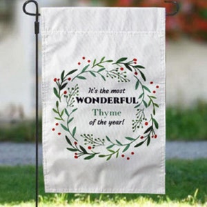 May include: White garden flag with a green wreath with red berries and the text "It's the most WONDERFUL Thyme of the year!"