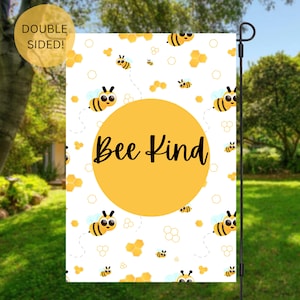 May include: A white garden flag with a yellow circle in the center that says "Bee Kind". The background is a white pattern of bees and honeycombs.