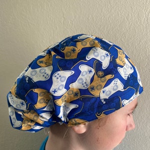 May include: Blue and white surgical scrub hat with a pattern of yellow and white video game controllers.