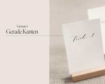 Könnte beinhalten: Weiße Karte mit dem Text "Tisch 1" in schwarzer Kalligraphie auf einem Holzständer. Die Karte liegt auf einer beigefarbenen Oberfläche.