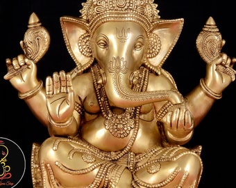 May include: A gold-colored brass statue of Ganesha, the Hindu god of wisdom and prosperity. The statue depicts Ganesha sitting with his trunk raised and holding a conch shell in one hand and a sweet in the other. The statue is intricately detailed and features a rat at the base.