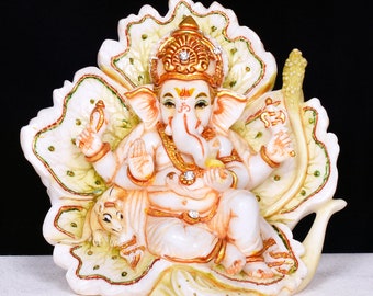 May include: White marble statue of Ganesha, the Hindu god of wisdom and prosperity, sitting on a lotus flower. The statue is decorated with gold paint and rhinestones. The god is holding a small object in his right hand and a lotus flower in his left hand. A small mouse is sitting at the base of the statue.