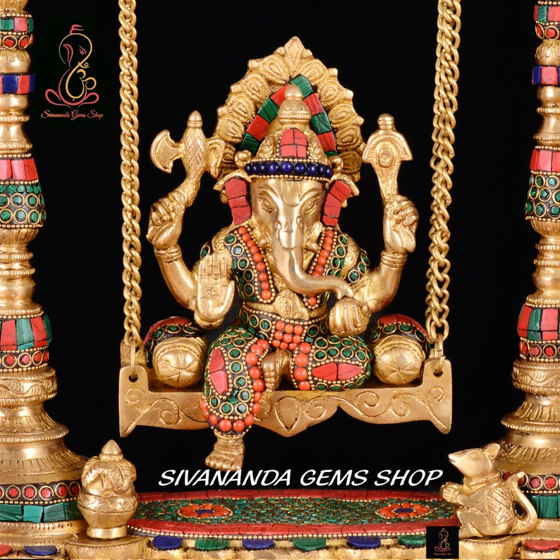 May include: A gold-colored statue of Ganesha, the Hindu god of wisdom and prosperity, sitting on a swing. The statue is decorated with colorful gemstones and intricate details. The swing is made of gold chains and has a decorative base.