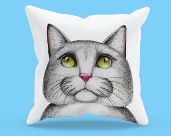 May include: A white pillow with a gray cat face printed on it. The cat has green eyes and a pink nose.
