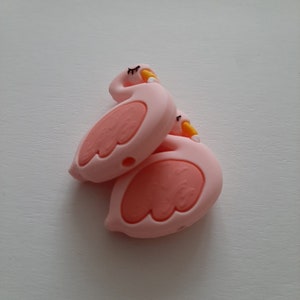 May include: Two pink silicone flamingo toys with yellow beaks and black eyes. The toys are stacked on top of each other.
