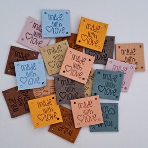 Op de afbeelding: Een stapel kleurrijke vierkanten van vilt met de tekst "Made with Love" en een hartvormig ontwerp. De vierkanten hebben gaten in de hoeken om te naaien.