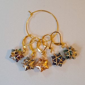 Könnte beinhalten: Satz mit fünf goldenen Stern-Maschenmarkierern mit schillernden Glasperlen. Jeder Marker hat einen goldenen Ring und einen goldenen Haken.