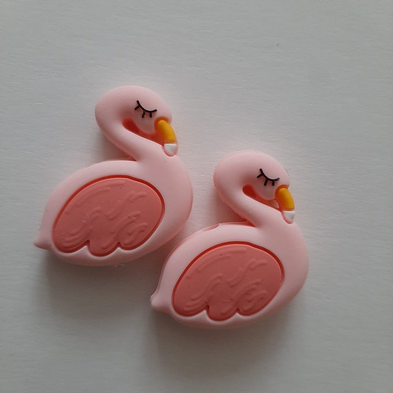 May include: Two pink silicone flamingo shaped baby teethers with closed eyes and yellow beaks.