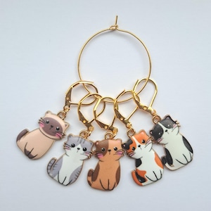 May include: Set of six gold cat stitch markers with different colored cats. The markers are attached to a gold ring.