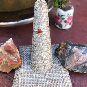 May include: A silver ring with a small, round, red gemstone set in the center.