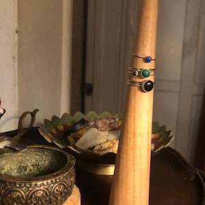 May include: A wooden ring holder with four rings on it. The rings have blue, green, and black stones.
