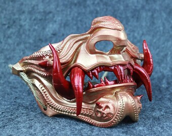 May include: A gold and red Oni mask with intricate details and sharp teeth. The mask is made of plastic and has a string for attaching it to the head.