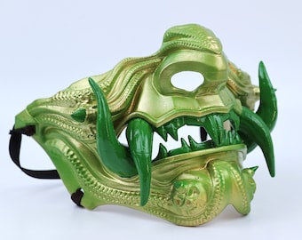 May include: A green and gold Oni mask with sharp teeth and horns. The mask has a strap for wearing.