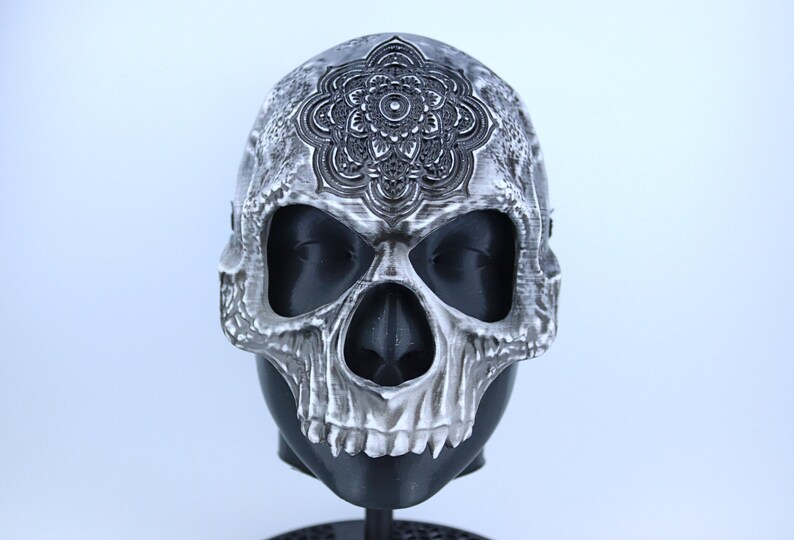 Pode incluir: Uma m&aacute;scara de caveira branca com um design de mandala detalhado na testa. A m&aacute;scara &eacute; feita de pl&aacute;stico e tem um aspecto realista.