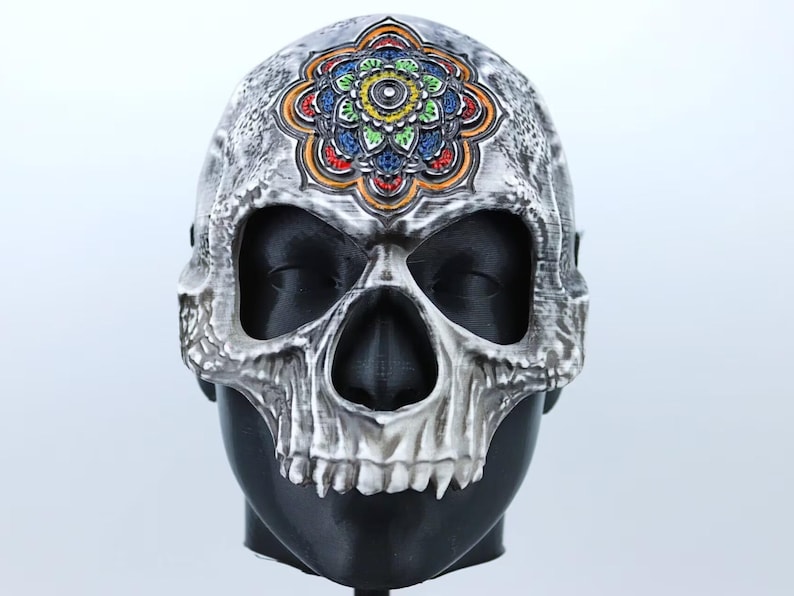 Pode incluir: Uma m&aacute;scara de caveira branca com um design de mandala colorido na testa. A m&aacute;scara tem uma superf&iacute;cie detalhada e texturizada e &eacute; feita de um material r&iacute;gido.