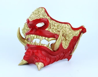 May include: A red and gold Oni mask with sharp teeth and horns. The mask is made of plastic and has a textured surface.