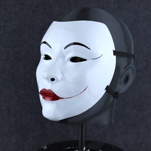 May include: A white mask with a black outline and a red smile. The mask is on a black mannequin head.