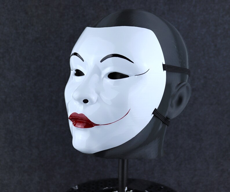 May include: A white mask with a black outline and a red smile. The mask is on a black mannequin head.