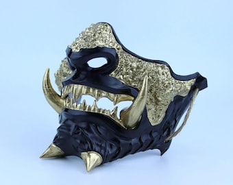 May include: A black and gold Oni mask with sharp teeth and horns. The mask is made of plastic and has a textured surface.