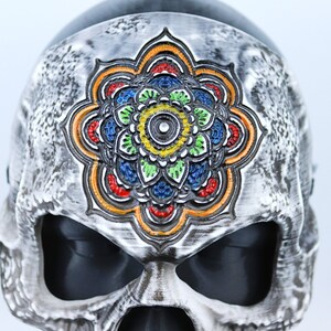 Pode incluir: Uma m&aacute;scara de caveira branca com um design de mandala colorido na testa. O mandala &eacute; pintado em tons de vermelho, laranja, amarelo, verde, azul e preto.