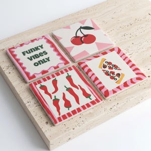 May include: A set of four square coasters featuring distinct designs: one with the text FUNKY VIBES ONLY in dark green, one with a red cherry illustration on a pink starburst, one with red chilli peppers, and one with a slice of pizza with toppings.