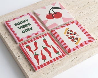 May include: A set of four square coasters featuring distinct designs: one with the text FUNKY VIBES ONLY in dark green, one with a red cherry illustration on a pink starburst, one with red chili peppers, and one with a slice of pizza with toppings.
