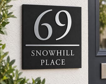 May include: A square black house sign featuring the large silver number 69 at the top, followed by a horizontal silver line and the text SNOWHILL PLACE in silver capital letters, mounted on a textured white wall surface.
