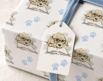 May include: A white gift box wrapped in paper featuring a repeating illustration of a light brown dog wearing black glasses and reading an open book, accented by light blue paw prints and tied with a light blue velvet ribbon and a matching gift tag.