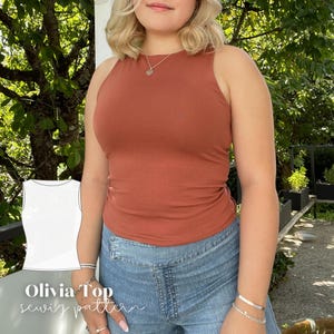 May include: A rust-colored tank top with a high neckline is worn with blue denim jeans. The image includes a white line drawing of the tank top and the text "Olivia Top sewing pattern". The top is form-fitting and appears to be made of a soft material.
