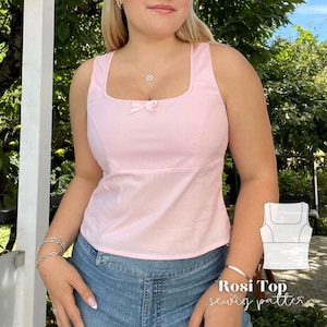 May include: A pink sleeveless top with a square neckline and a bow at the centre. The top is made of a soft, lightweight fabric and has a fitted silhouette. The model is wearing the top with a pair of blue jeans.