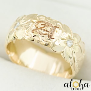 Pode incluir: Uma aliança de ouro com um design floral e um único diamante. A aliança é gravada com a letra "A".