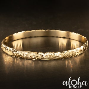 May include: A gold bangle bracelet with a floral design. The bracelet is made of 14k gold and is a popular choice for Hawaiian jewelry.
