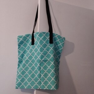 Può includere: Una borsa tote color turchese con un motivo geometrico bianco. La borsa ha manici neri.