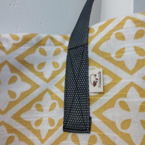 Może przedstawiać: Mata do jogi z żółtym i białym wzorem, z czarnym paskiem i białą etykietą z napisem "Handmade".