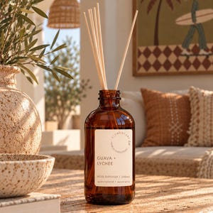 May include: A brown glass reed diffuser bottle with a white label reading Elementary Co. Earth Conscious Guava + Lychee Reed Diffuser 200ml Queensland Australia. Several light-coloured wooden reeds are inserted into the bottle opening.