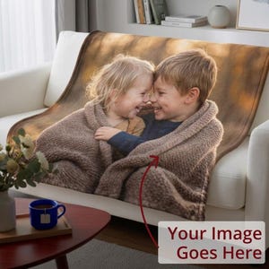 May include: A personalized blanket featuring a warm, brown-toned image of two children wrapped in a knitted blanket, smiling and embracing. The blanket is draped over a white sofa. Text at the bottom reads "Your Image Goes Here."