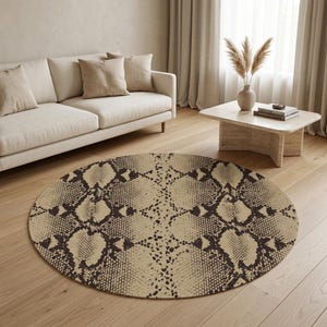 Op de afbeelding: Een ronde vloerkleed met een slangenprint in bruin- en beigetinten. Het kleed ligt op een lichte houten vloer in een woonkamer. Een beige bank en salontafel zijn ook zichtbaar.