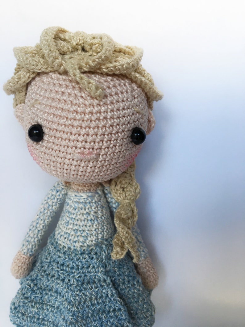 K&ouml;nnte beinhalten: Eine geh&auml;kelte Puppe mit blonden Haaren, einem blau-wei&szlig;en Kleid und schwarzen Augen.