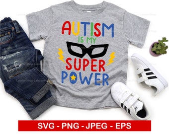 May include: A gray t-shirt with the text "AUTISM IS MY SUPER POWER" in colorful letters. A black superhero mask is above the text. The shirt is on a white background with a pair of white sneakers and a potted plant.