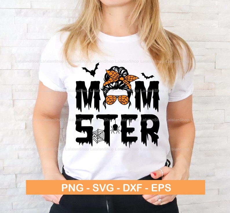 Puede incluir: Una camiseta blanca con un gr&aacute;fico negro y naranja que dice "Momster" con una imagen de dibujos animados de una mujer con un mo&ntilde;o desordenado, gafas de sol y una diadema. El dise&ntilde;o tambi&eacute;n incluye murci&eacute;lagos y una telara&ntilde;a.