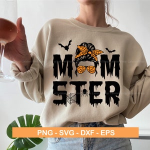 Puede incluir: Una sudadera beige con un dise&ntilde;o gr&aacute;fico negro que dice "Momster" con una ara&ntilde;a negra y una telara&ntilde;a. El gr&aacute;fico tambi&eacute;n incluye una imagen de dibujos animados de una mujer con un mo&ntilde;o desordenado, gafas de sol y un pa&ntilde;uelo. El texto gotea con un l&iacute;quido negro.