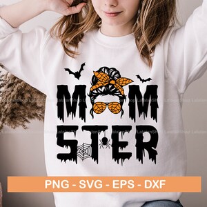 Puede incluir: Una sudadera blanca con un dise&ntilde;o gr&aacute;fico negro y naranja que dice "Momster" con una telara&ntilde;a y una ara&ntilde;a. El gr&aacute;fico presenta a una mujer con un mo&ntilde;o desordenado y gafas de sol.