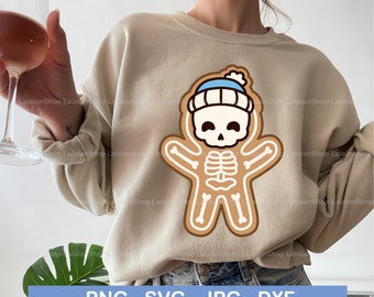 Pode incluir: Uma camisa de moletom bege com um esqueleto de gengibre de desenho animado usando um chapéu azul e branco. O esqueleto está sorrindo e tem uma caveira na cabeça.