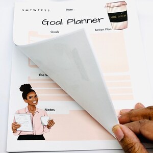 Peut inclure: Un planificateur de buts rose et blanc avec une illustration de tasse &agrave; caf&eacute; qui dit "Girl Boss". Le planificateur comporte des sections pour les objectifs, le plan d'action et les notes. Une femme &agrave; la peau fonc&eacute;e est illustr&eacute;e tenant une tasse &agrave; caf&eacute; et un planificateur.