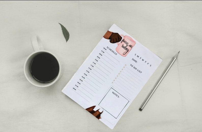 May include: A white planner with a pink and brown illustration of a hand holding a mug with the text "focus on today". The planner has sections for a schedule, to-do list, and notes.