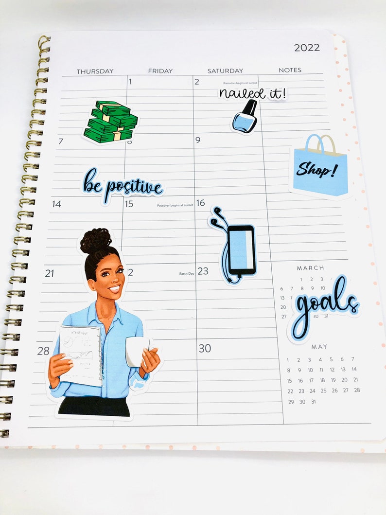 May include: A monthly planner with stickers. The stickers include a stack of money, a nail polish bottle, a shopping bag, a woman with a coffee cup and a book, and a calendar with the word "goals" written on it.