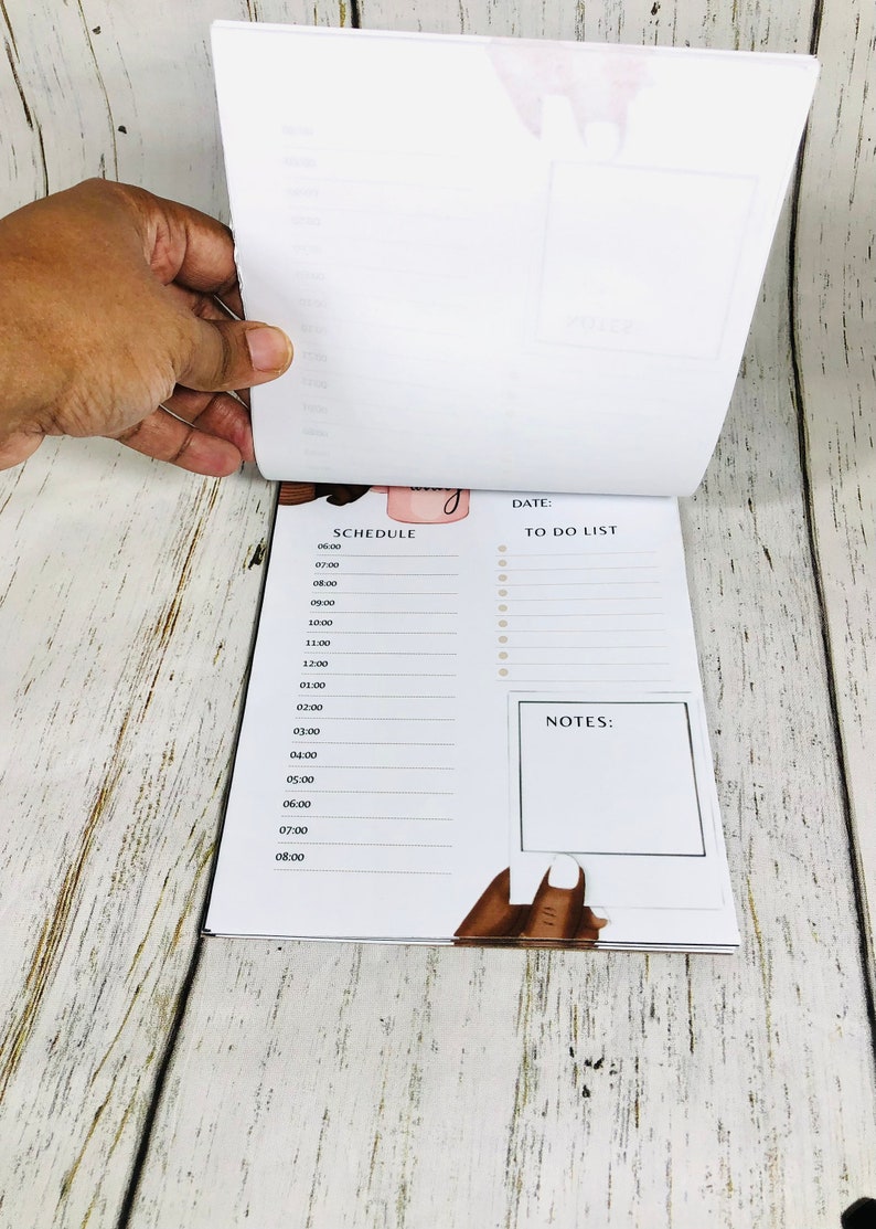 May include: A white planner with a black and white illustration of a woman's hand with a manicure. The planner has a section for a daily schedule, a to-do list, and notes.