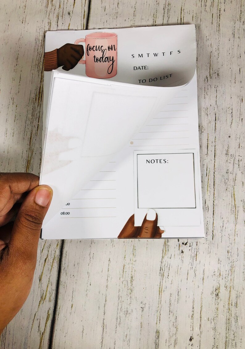May include: A white daily planner with a to-do list, notes section, and a calendar. The planner has a pink and white illustration of a hand holding a coffee mug with the text "focus on today".