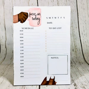 May include: A white daily planner with a pink coffee cup illustration and the text "focus on today". The planner has a schedule section with times from 6:00 AM to 8:00 PM, a to-do list section, and a notes section.